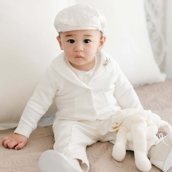 Baby sitting on a bed wearing the Oliver Quilted Jacket Suit with a matching cap and white stuffed bunny resting on their lap.