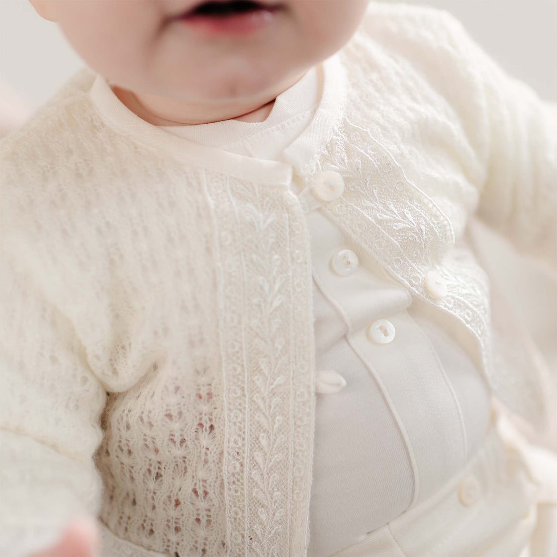 A close-up of the sweater’s delicate lace design, showing the intricate openwork knit and pearl buttons.