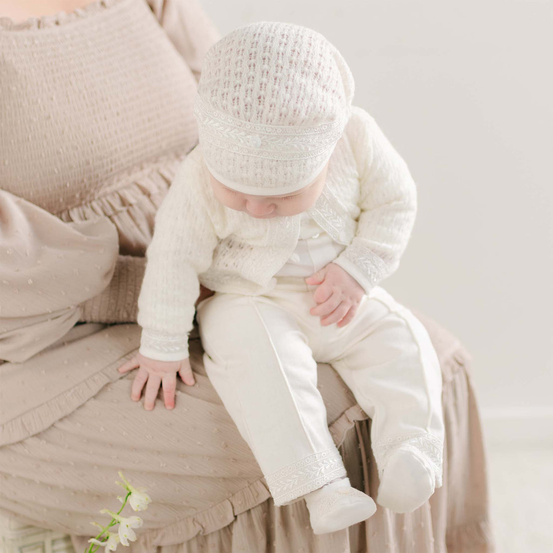 A baby looking down while wearing the Oliver Sweater Pants Suit, highlighting the intricate lace details on the sweater and pant cuffs.