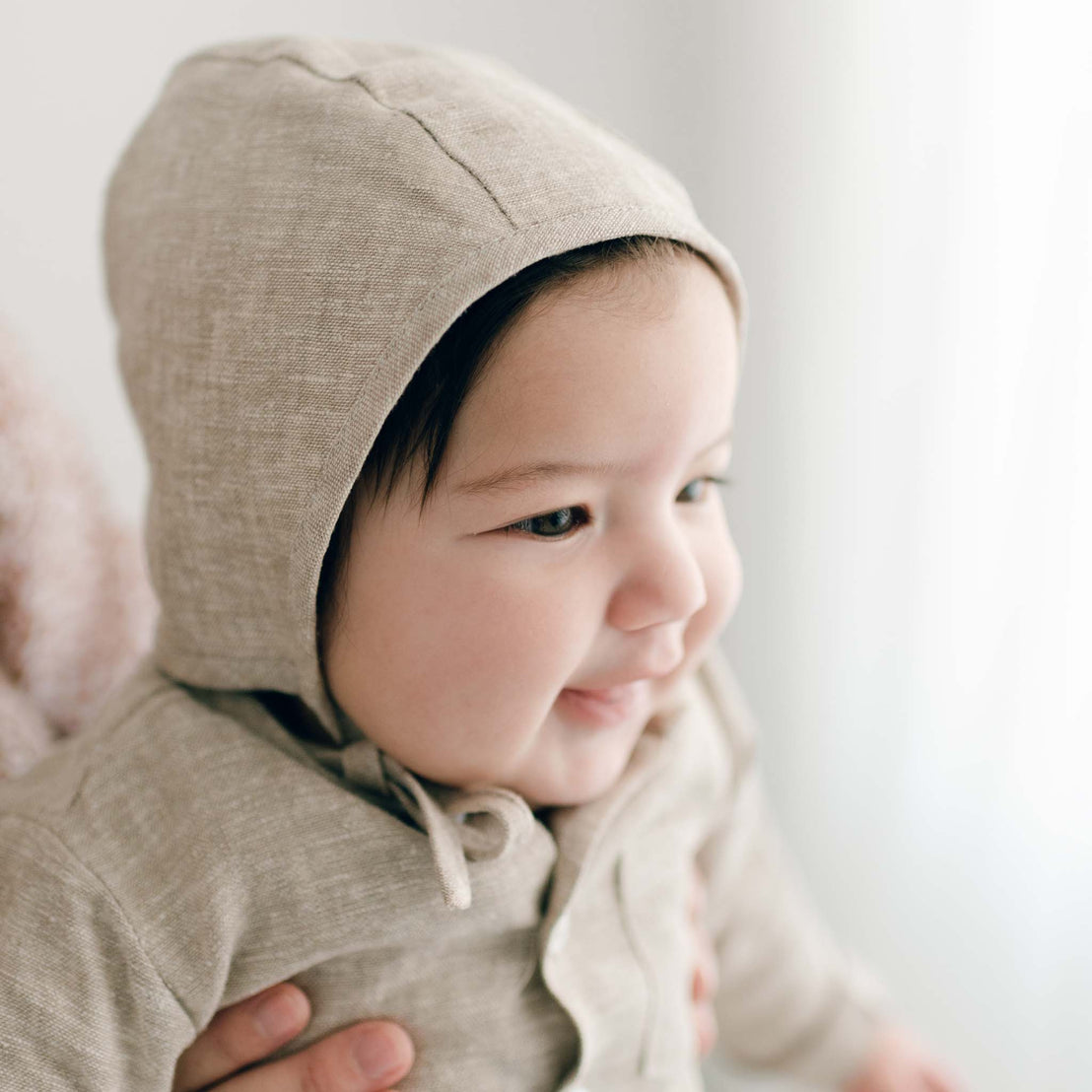Baby wearing a beige bonnet garment against a plain background
