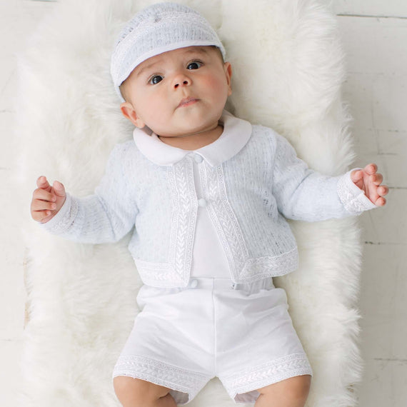 Baby in a blue knit sweater and matching white shorts lying on a white fur rug.