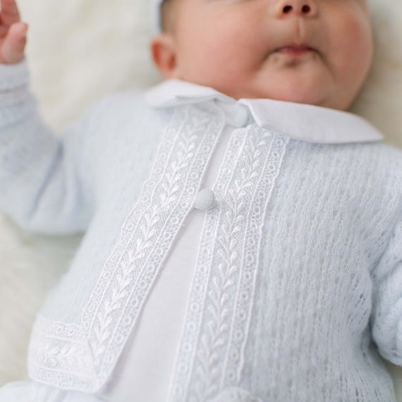 Baby wearing a light blue knit sweater with white lace trim.