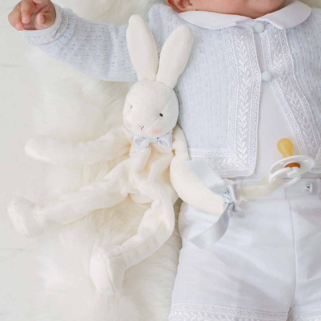 White plush bunny toy lying beside a baby in a white outfit.