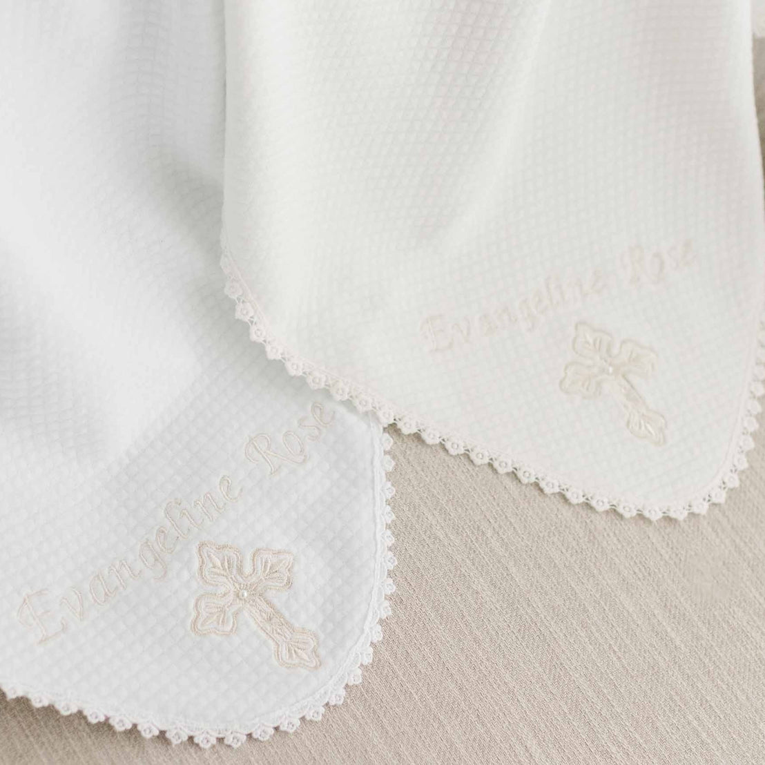 Two white personalized cross blankets embroidered with the name "Evangeline Rose" and a cross design, featuring intricate scalloped edges and an upscale heirloom quality.