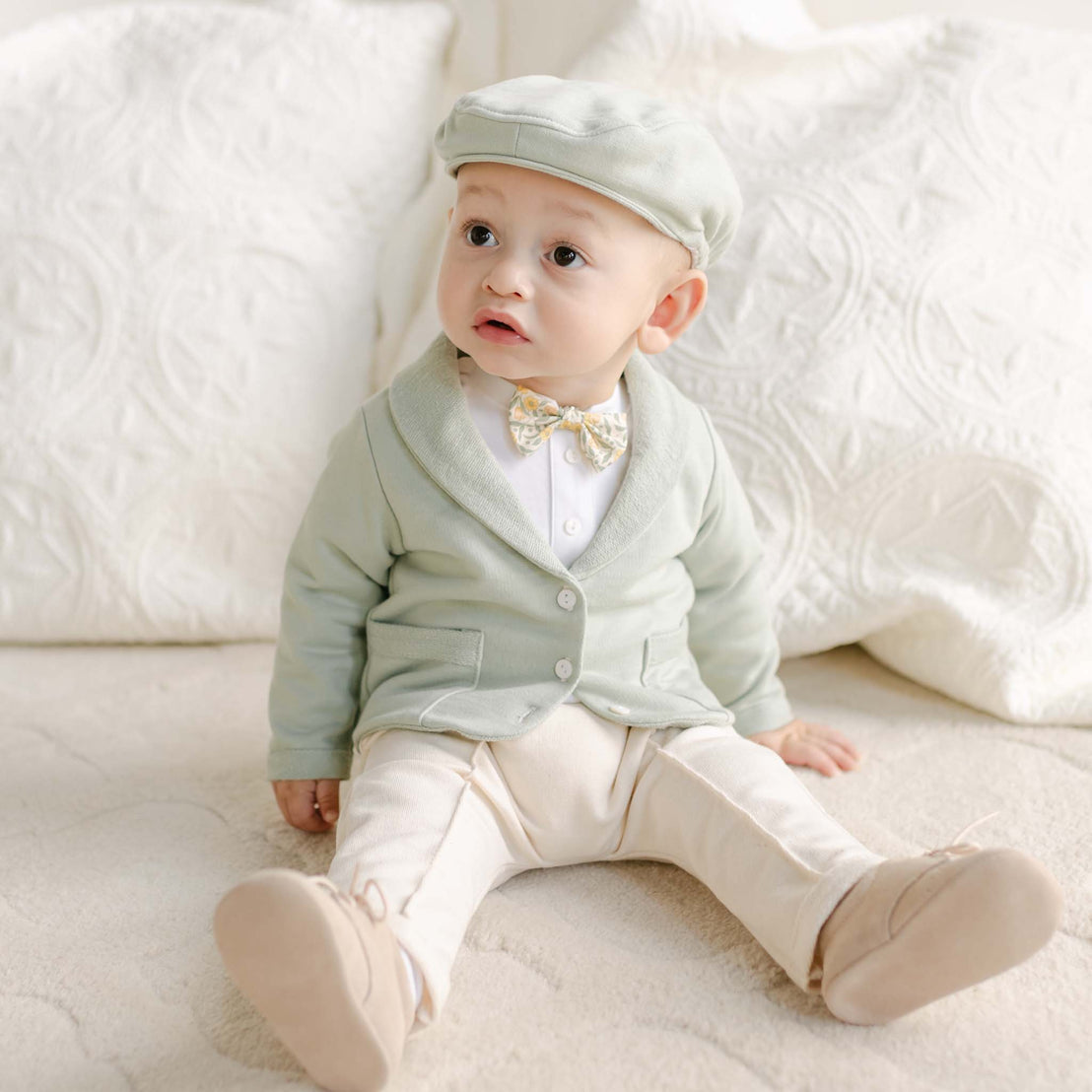 Seated baby in the Petite Fleur Yellow Bow Tie, green jacket, ivory pants, and soft shoes.