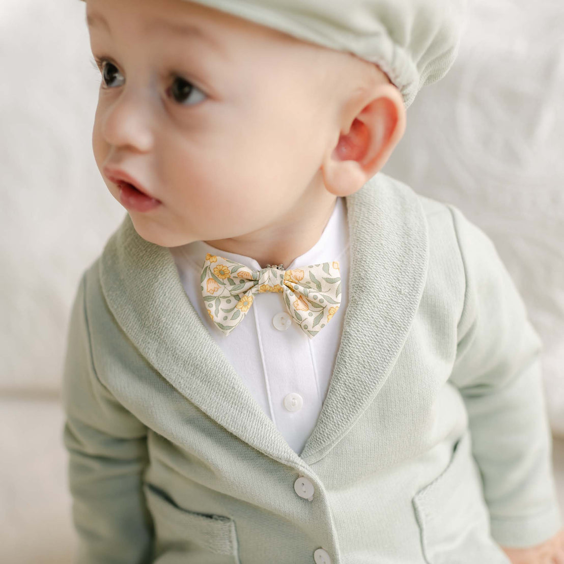 Baby in the Petite Fleur Yellow Bow Tie with a pale green jacket and matching cap.