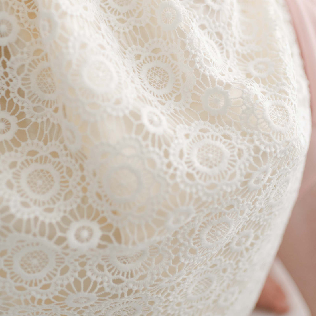 Close-up view of the intricate floral lace fabric of the Poppy Christening Gown, showcasing its delicate circular patterns and soft texture.