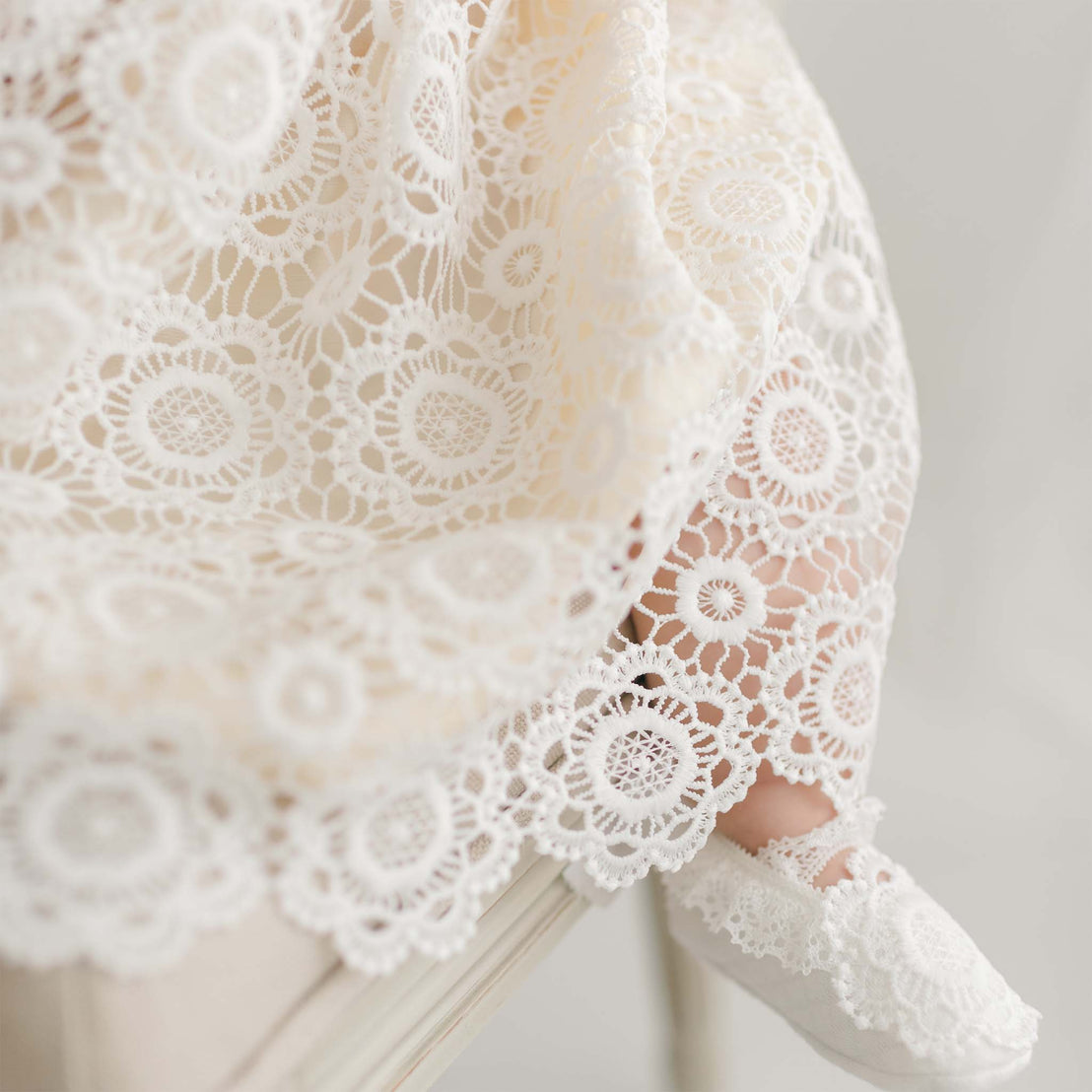 Close-up of the Poppy Dress's skirt and booties, highlighting the intricate floral lace overlay and lace-trimmed baby booties.