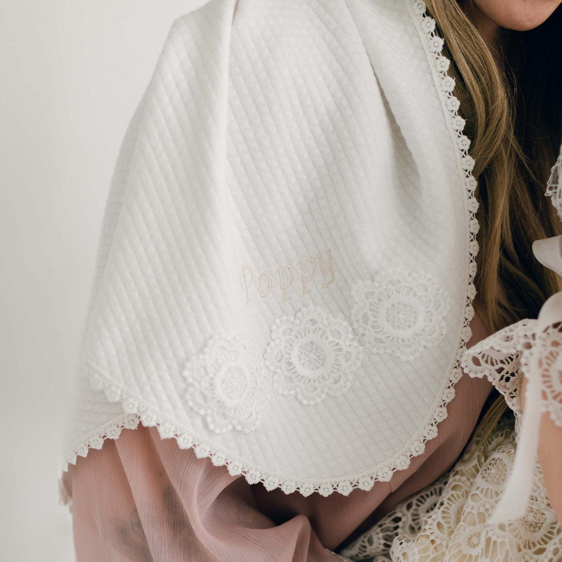 Close-up of the Poppy Personalized Blanket in soft quilted fabric, embroidered with the name 'Poppy' and adorned with delicate floral lace trim.