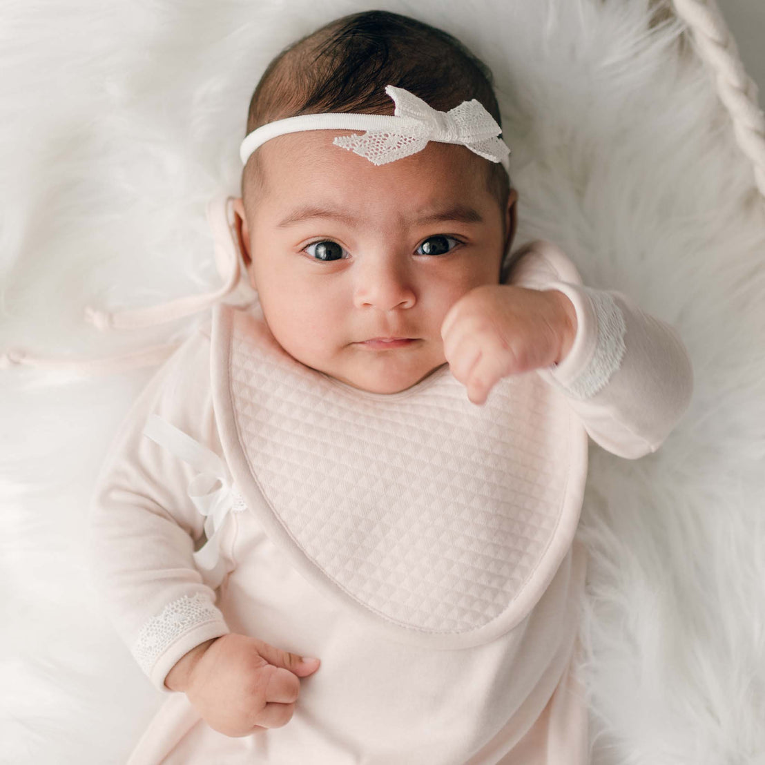 Baby boy wearing pink quilted cotton bib and lace bow headband.