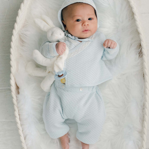 Baby boy blue cotton wrap top, pants and bonnet with bunny laying in basked