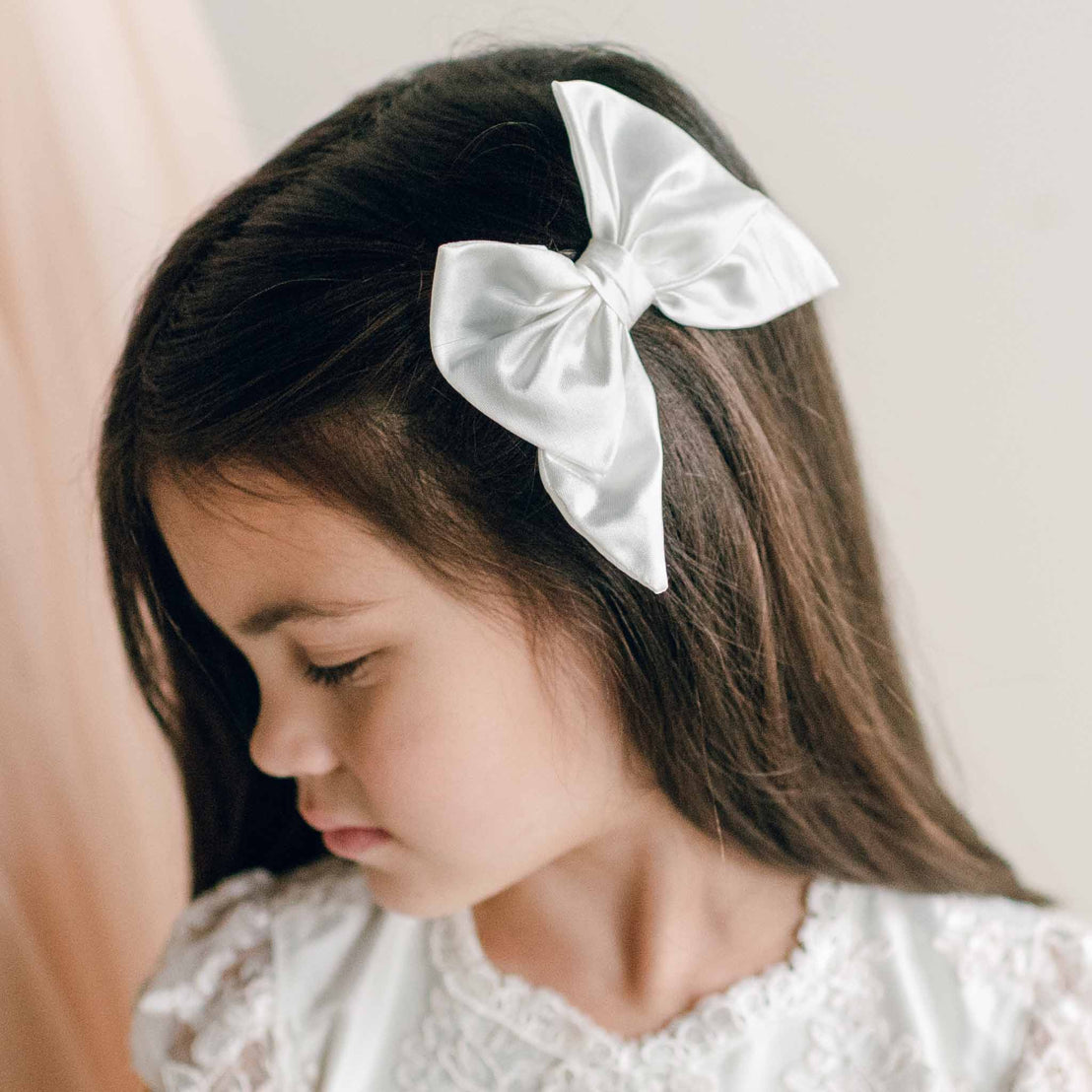 Girl wearing the Silk Bow Clip in white satin, styled on the side of her long dark hair.