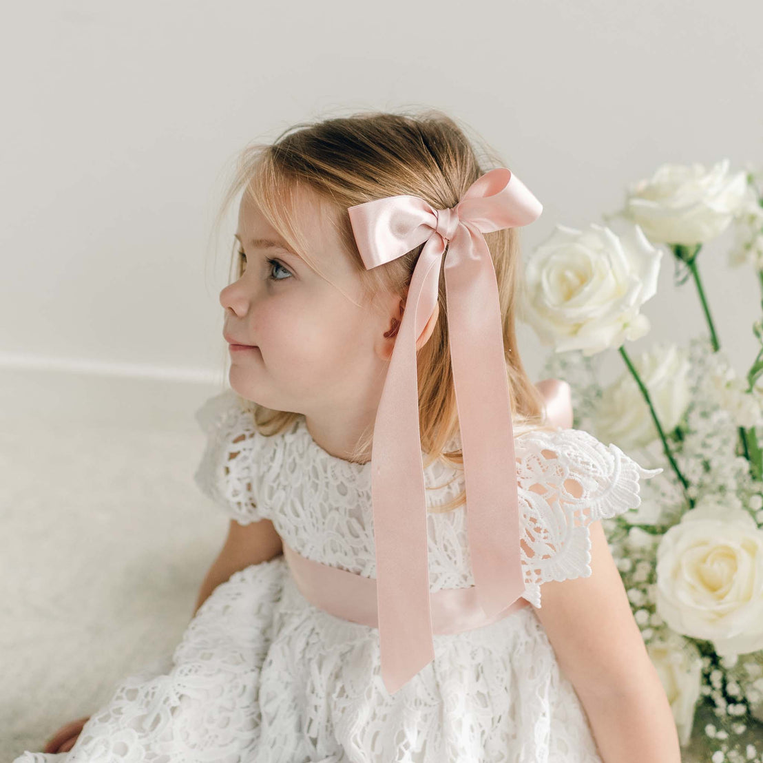 A blush pink silk ribbon hair bow styled to the side of a girl's hair.