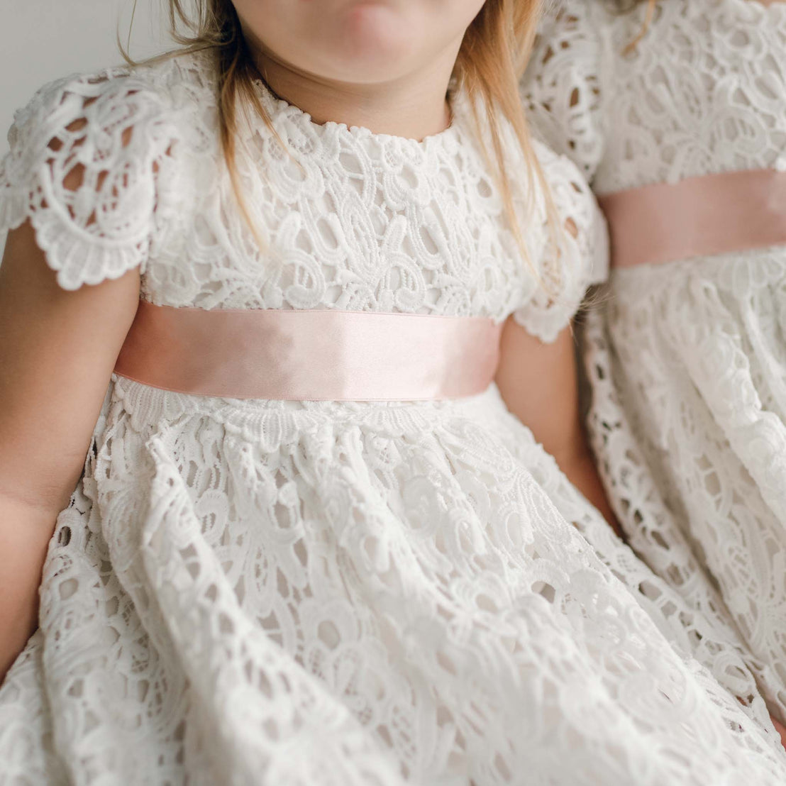 A close-up of a blush pink silk sash tied around a white lace dress.