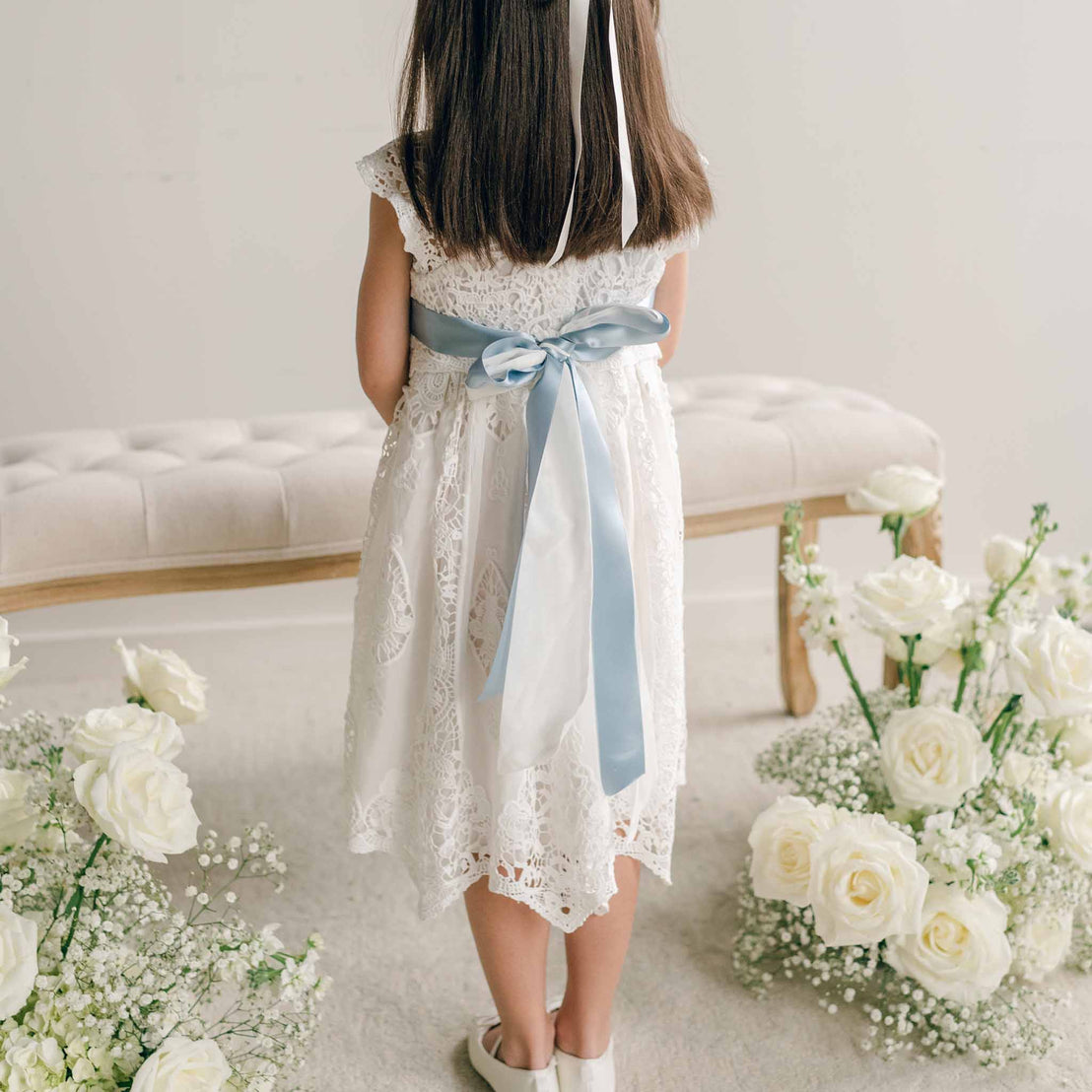 The back of a blue silk sash tied into a bow on a white lace dress.