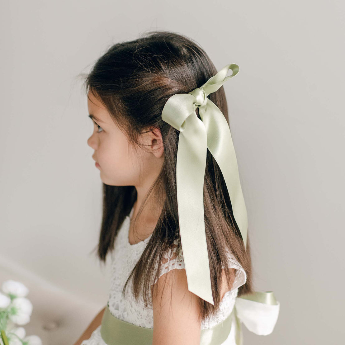 A sage green silk ribbon hair bow tied into the side of a girl's hairstyle.