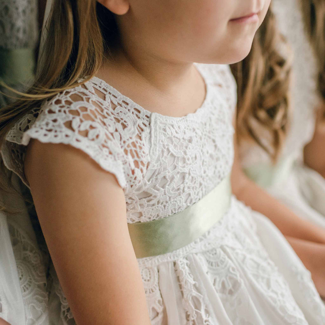 A detailed view of a sage green silk sash tied around a white lace dress.