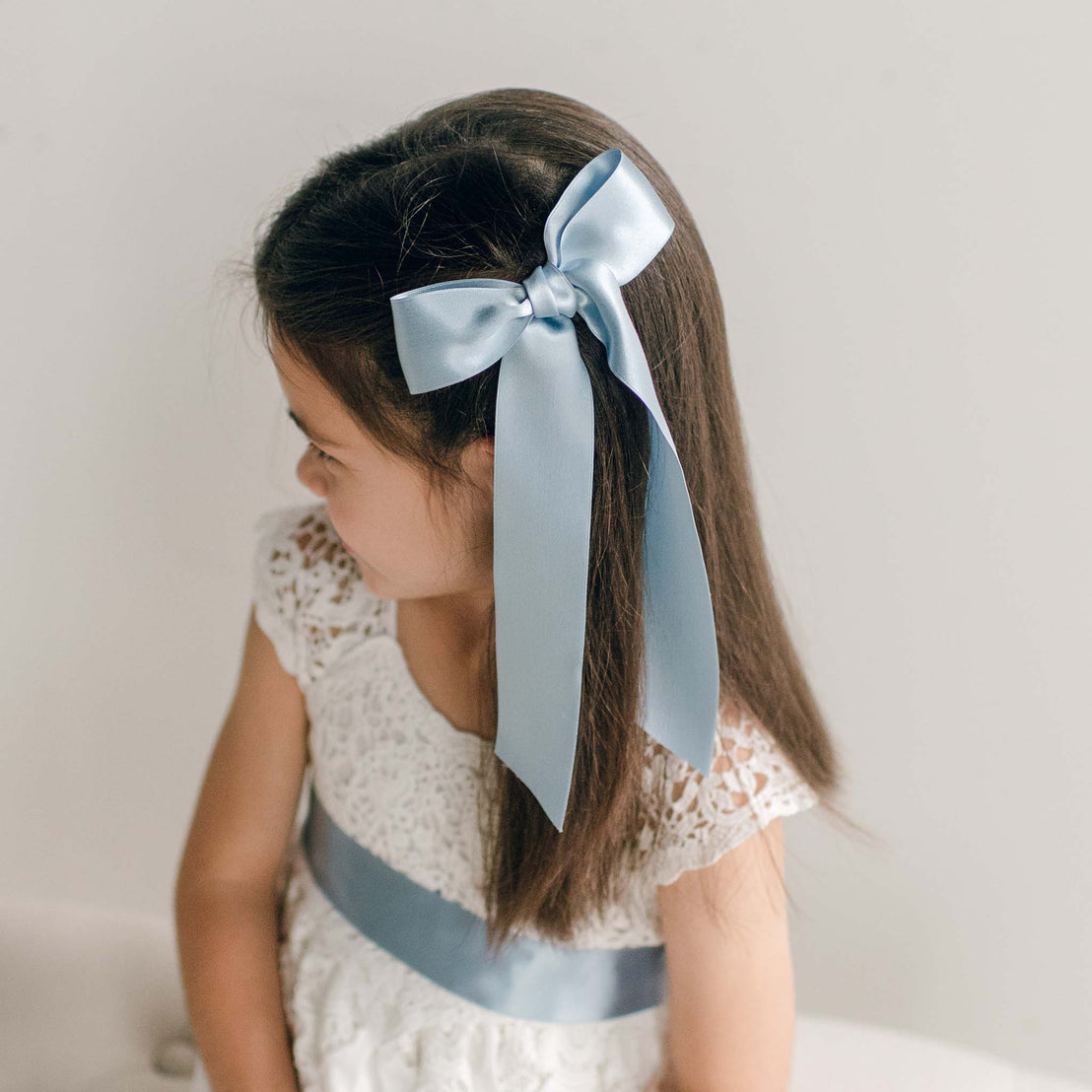 A girl wearing a blue silk ribbon hair bow, styled on the side of her straight hair.