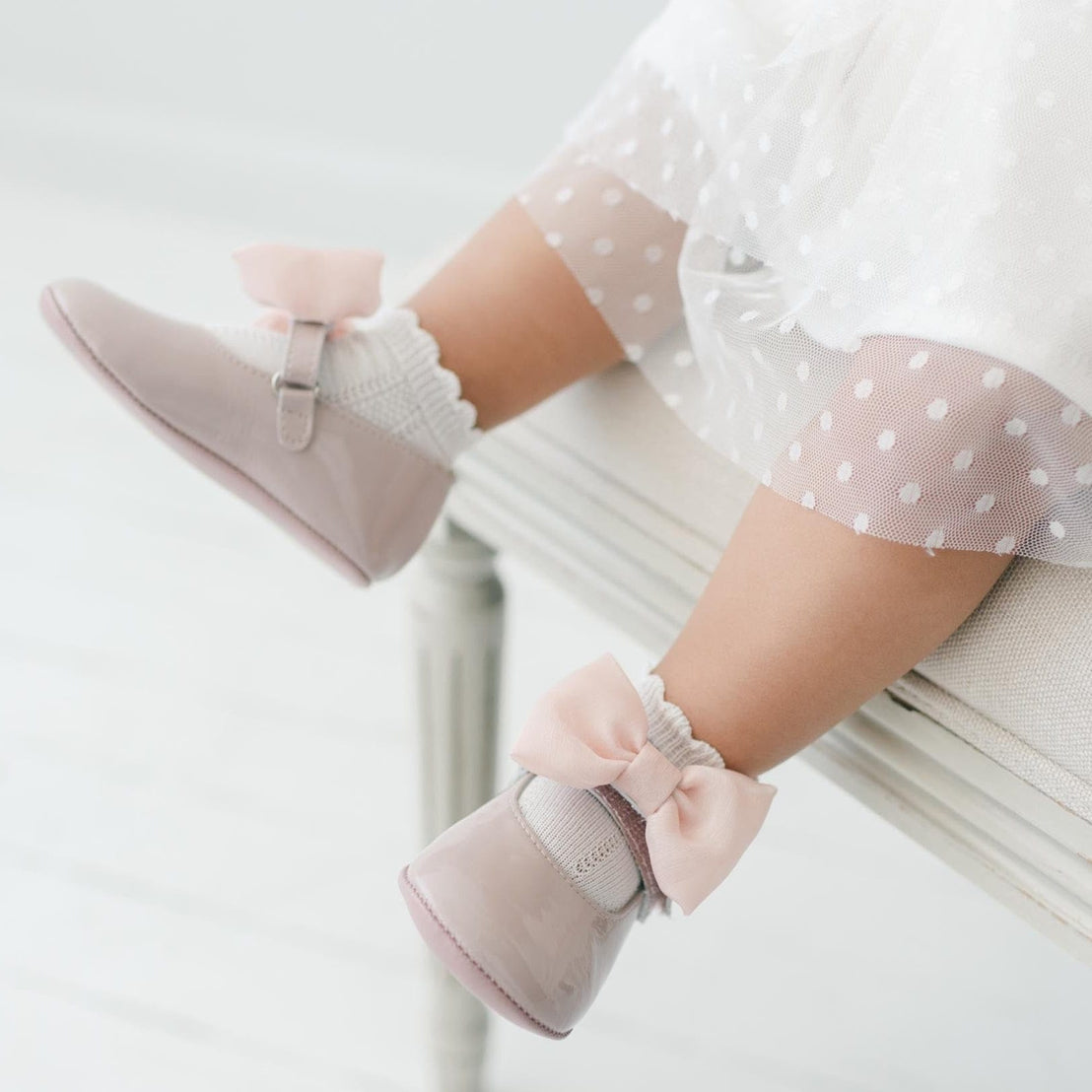 Baby's legs wearing pink Mary Jane shoes  with bows.