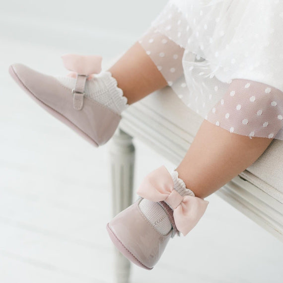 Baby's legs wearing pink Mary Jane shoes  with bows.