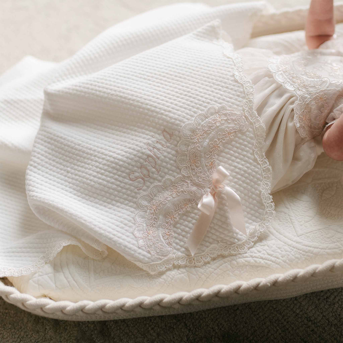 Close-up of the Sophia Blanket, featuring quilted white cotton with embroidered lace detailing, a delicate satin bow, and "Sophia" embroidered in soft blush thread.