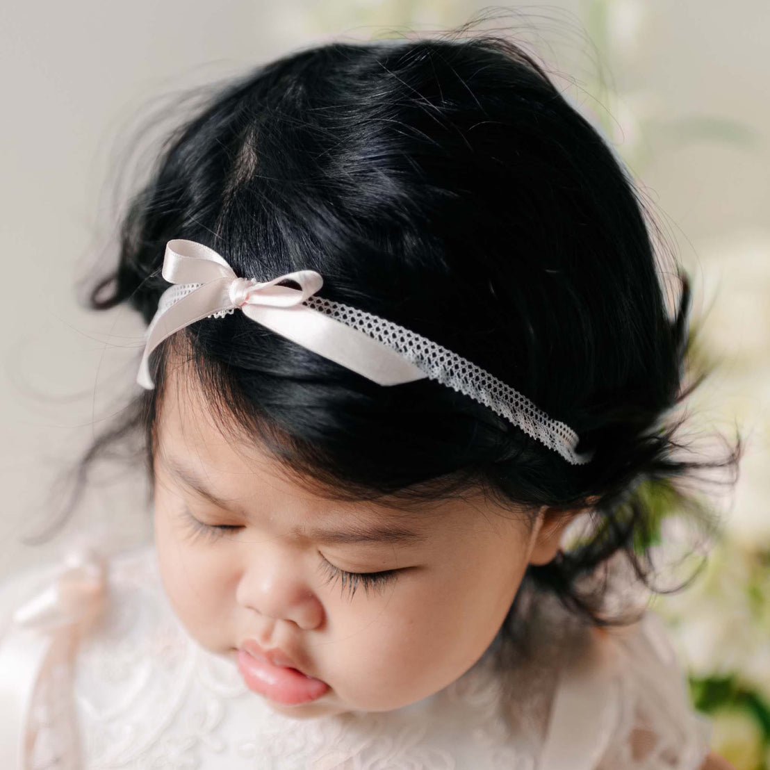 Close-up of the Sophia Silk Ribbon Headband on a baby's head, featuring a delicate satin bow and lace trim against dark hair.