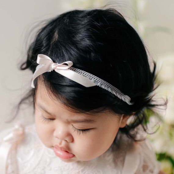 Close-up of the Sophia Silk Ribbon Headband on a baby's head, featuring a delicate satin bow and lace trim against dark hair.