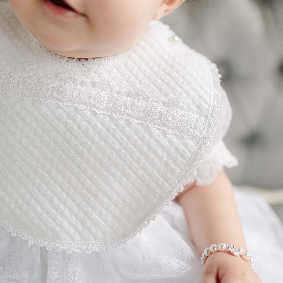 Close-up of a baby wearing a the Stella Bib. Close up details of the bib show a Venice lace on quilted cotton and white edge lace trim.