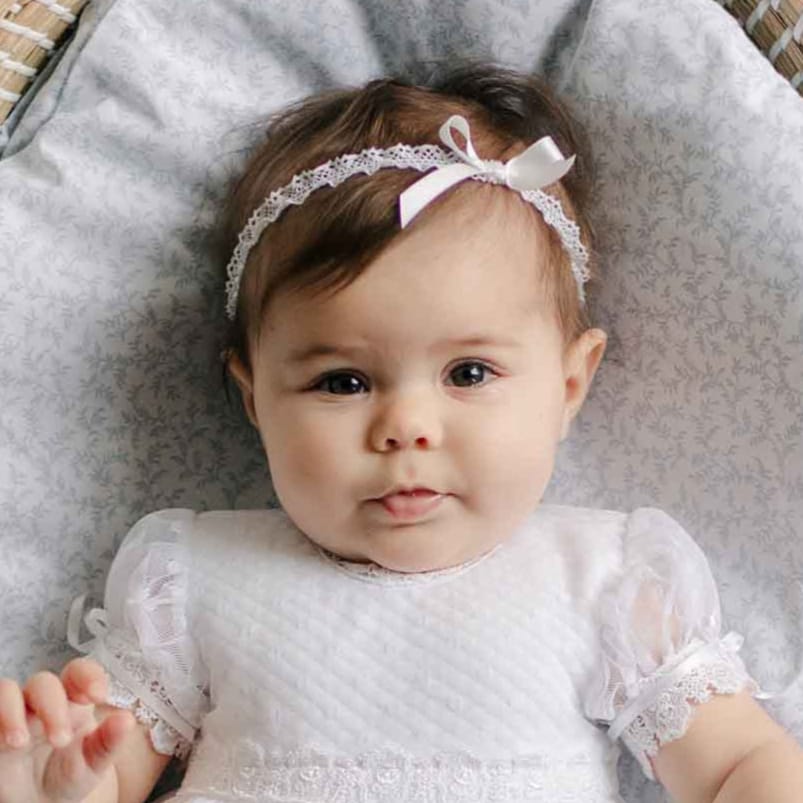 Baby wearing the Stella Silk Ribbon Headband and matching Dress against a patterned blanket. 