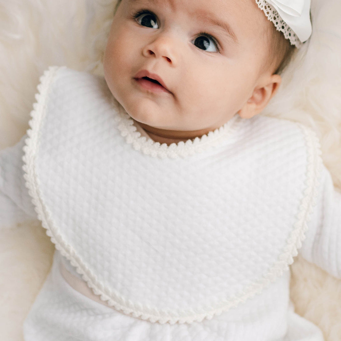 Newborn baby girl wearing the Tessa Quilt Bib made with a soft quilted cotton and accented with a floral edge lace.