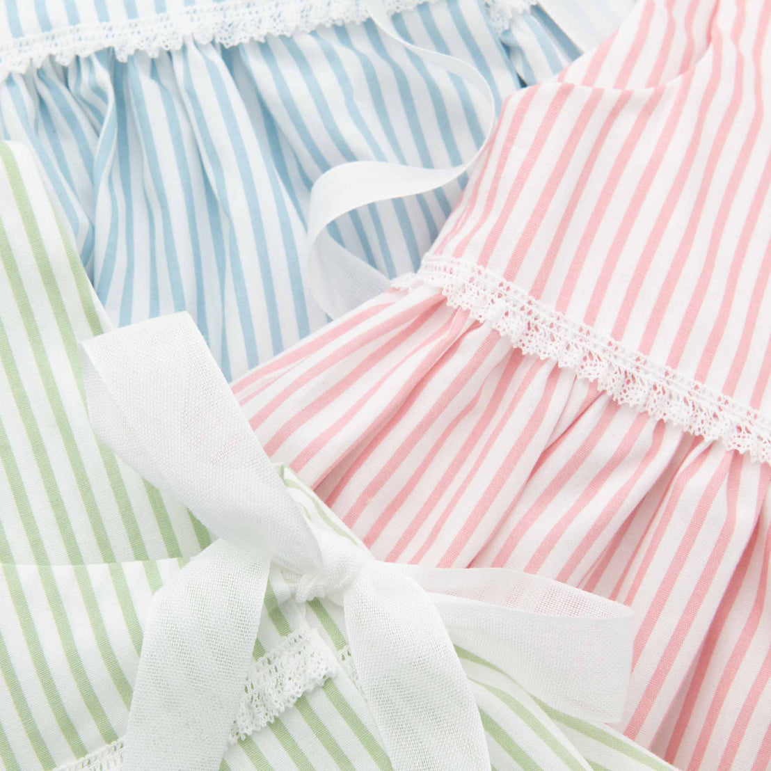 Close-up of three different Thea Wrap Dresses in shades of blue, pink, and green, each featuring delicate lace and ribbon details.