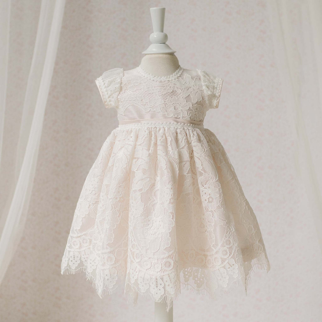 Full length view of the Victoria Dress on a mannequin against a neutral background. Details show the embroidered floral lace with cording and scalloped lace at the hems. Part of the Baby Beau & Belle Baptism Dresses Collection.
