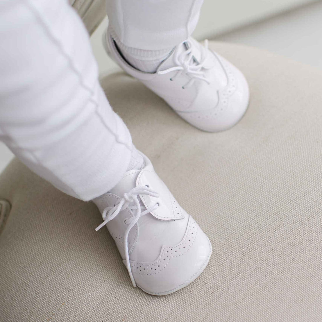White baby shoes worn with white pants on a light-colored floor.
