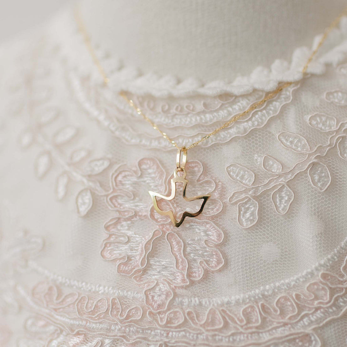 Gold necklace with a dove-shaped pendant on a lace fabric background