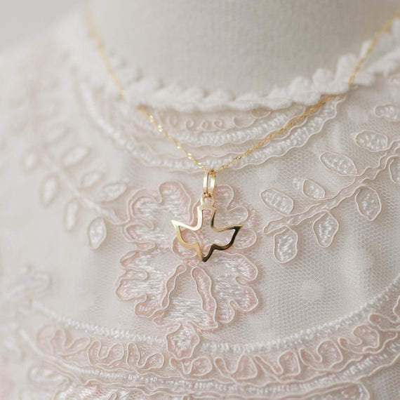 Gold necklace with a dove-shaped pendant on a lace fabric background
