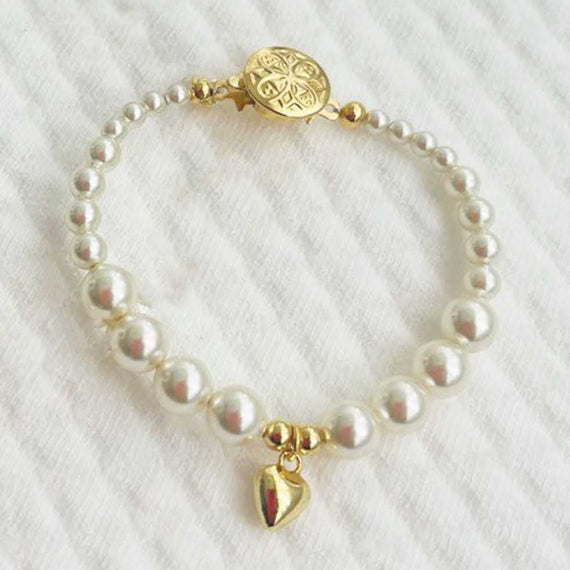 Cream pearl baby bracelet with gold plated heart charm on a white textured background