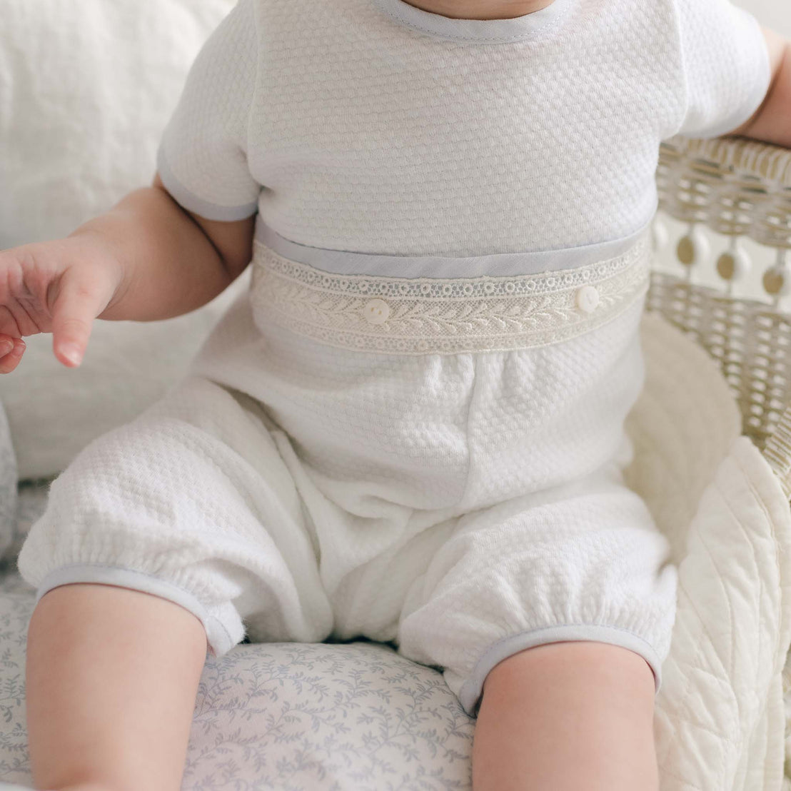 Close-up of the Harrison Short Sleeve Romper showcasing its textured quilted fabric, delicate lace detailing on the waistline, and soft light blue accents.