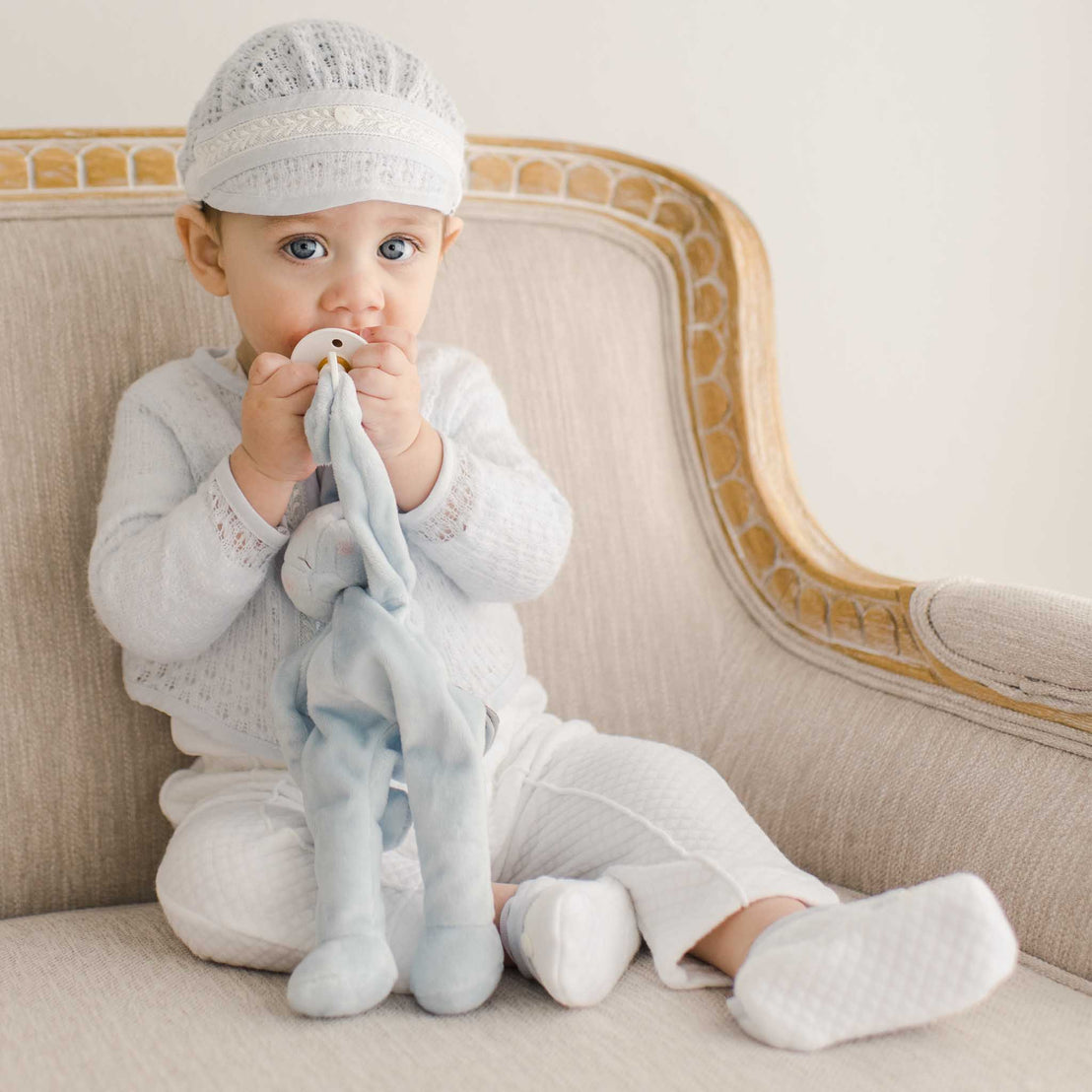 Baby boy sitting on a chair and wearing a Harrison 3-piece pant suit and matching blue knit sweater. He is holding a blue bunny stuffed animal pacifier holder