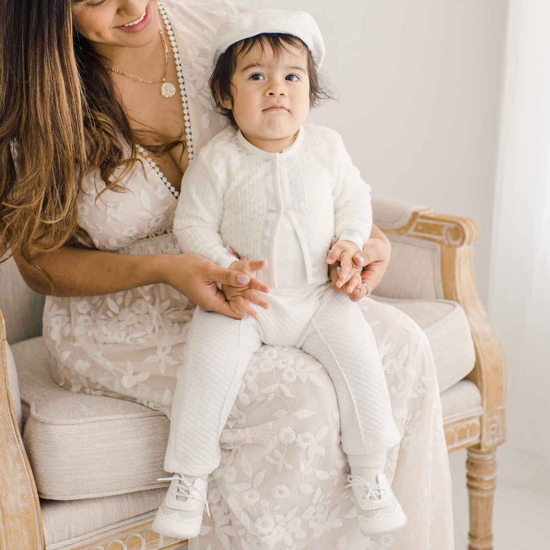 Baby boy sitting on the lap of his mother. He is wearing the Owen 3-Piece Suit, including the sweater, pants, and onesie