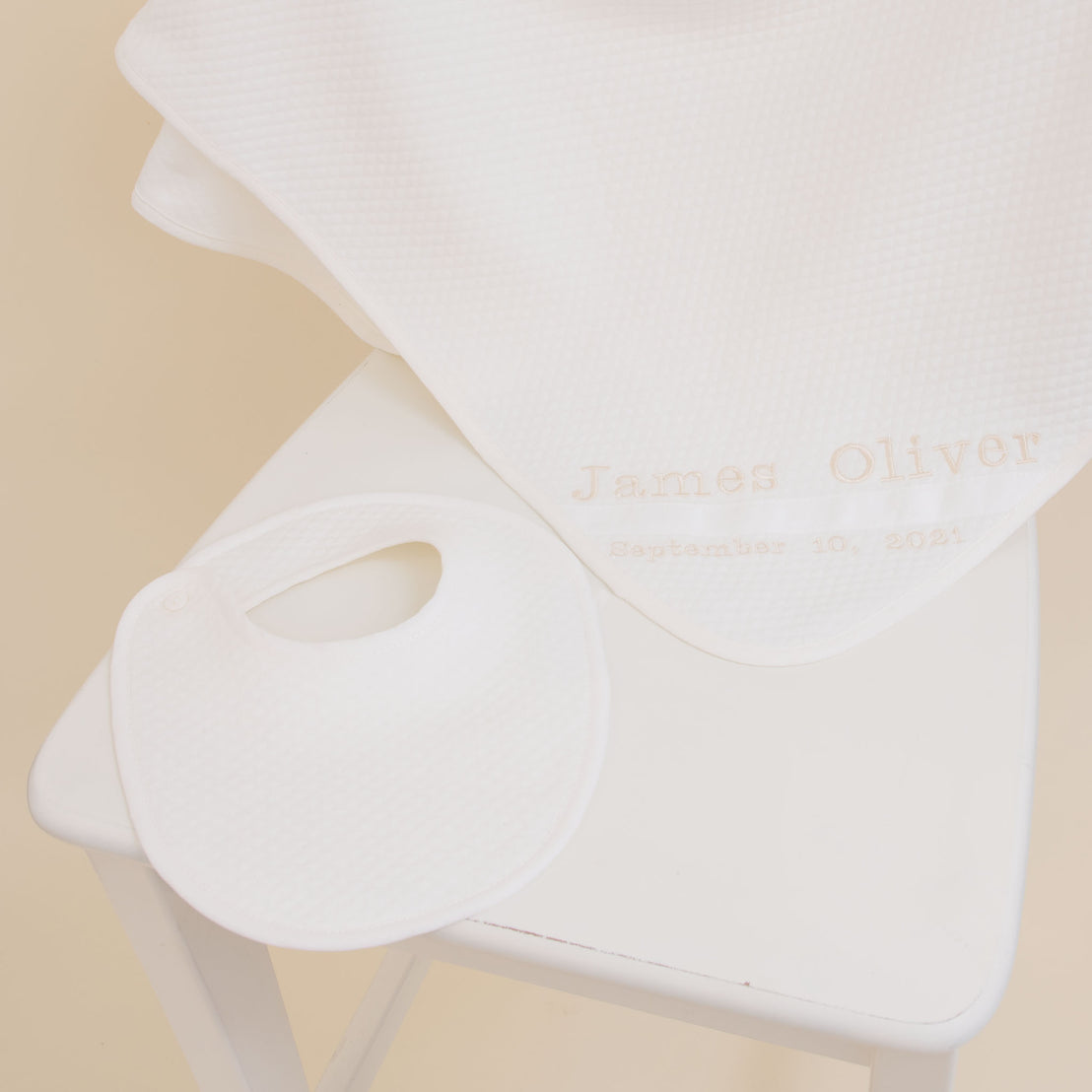 A Baby Beau & Belle Baby Boy Personalized Gift Set with the name "James Oliver" and the date "September 10, 2021," embroidered as a keepsake, resting on a white chair with a soft fabric backdrop