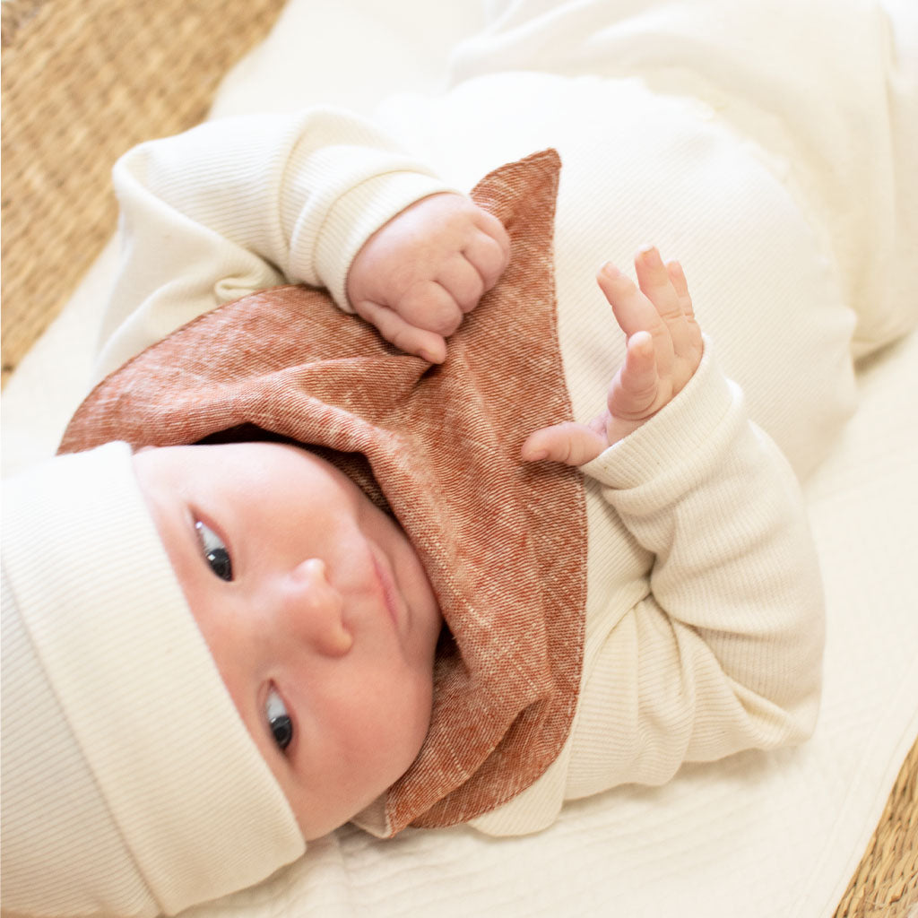 Baby boy wearing the clay colored Silas Bandana Bib and laying in a woven basket