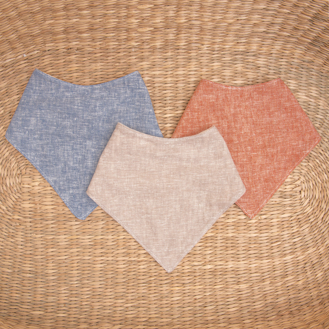 Flat lay photo of all three colors of the Silas Bandana Bib. The bibs are made from linen in three different colors: indigo, sand, and clay.
