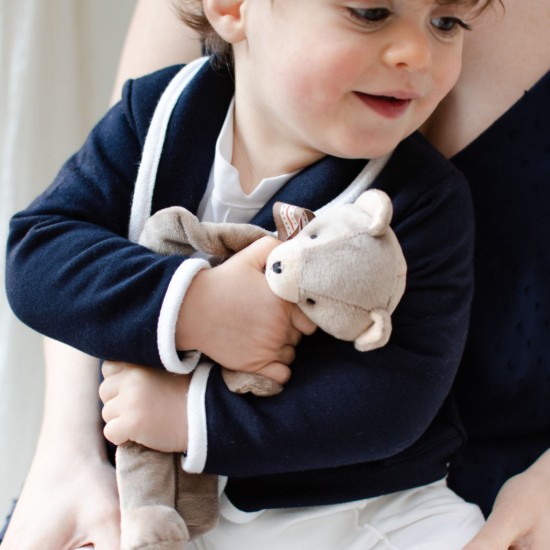 Baby boy holding on to a Elliott Bear Buddy, a floppy stuffed animal bear that clips on to a pacifier.