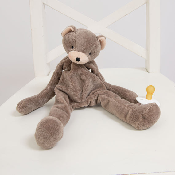 Flat lay photo of the Elliott Bear Buddy, a floppy stuffed animal bear that clips on to a pacifier.