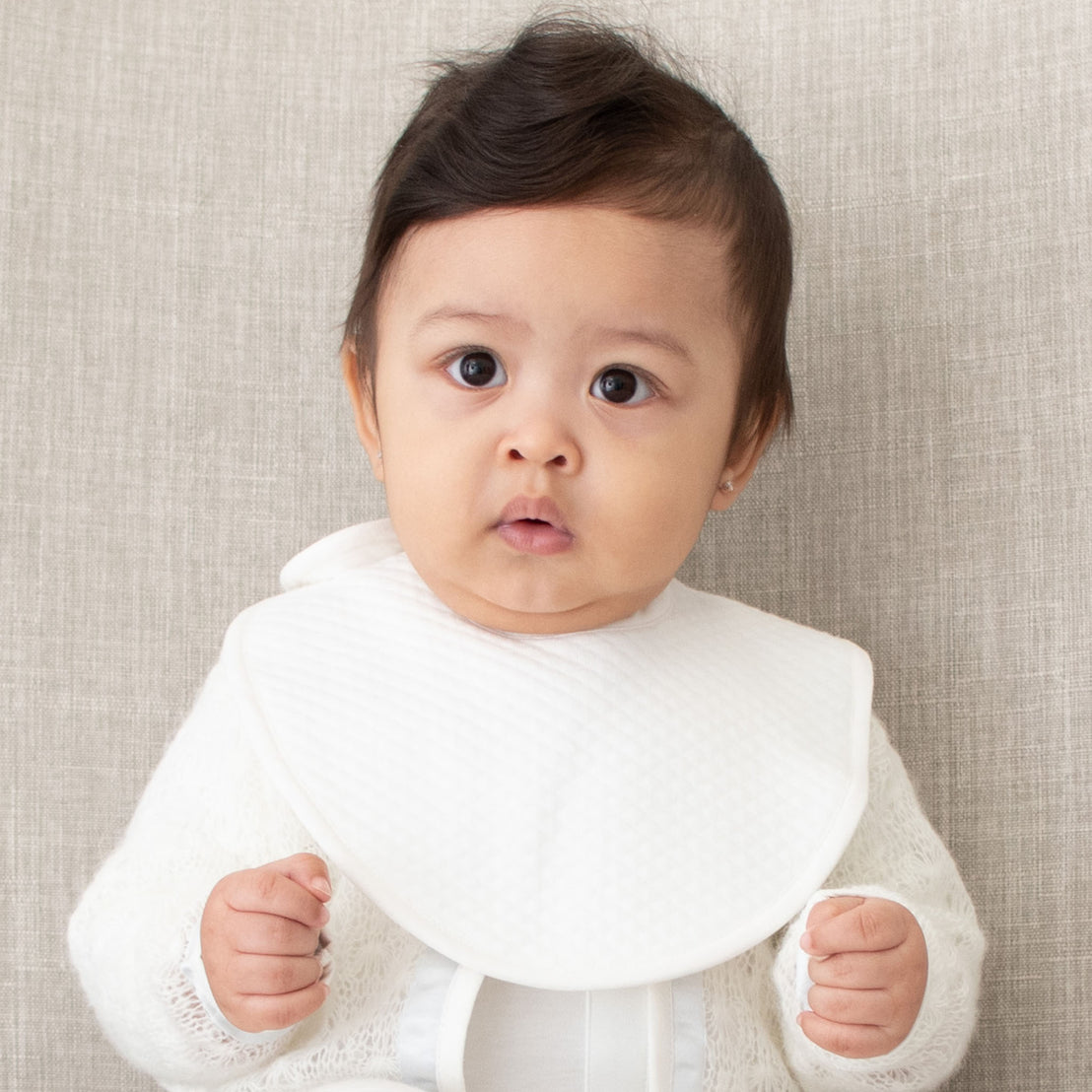 Closeup photo of a baby boy wearing the Owen Bib made out of ivory quilted cotton and an ivory linen trim.