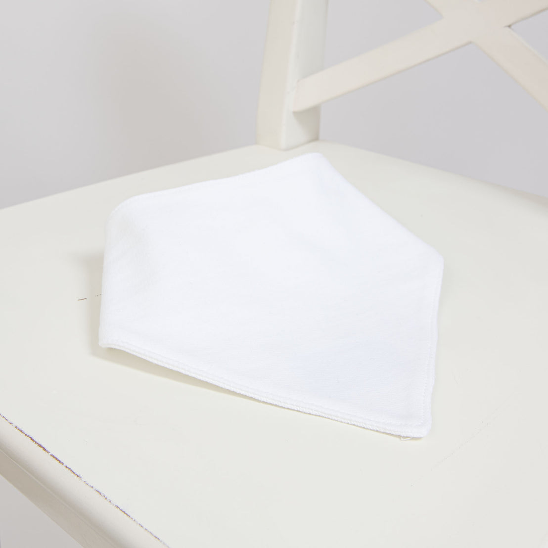 Flat lay photo of the Elliott Bib, made from white French Terry cotton, on a white chair.