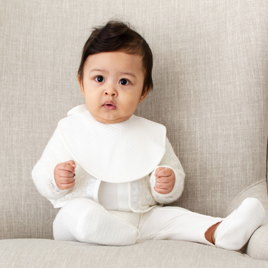 Photo of a baby boy wearing the Owen Bib made out of ivory quilted cotton and an ivory linen trim.
