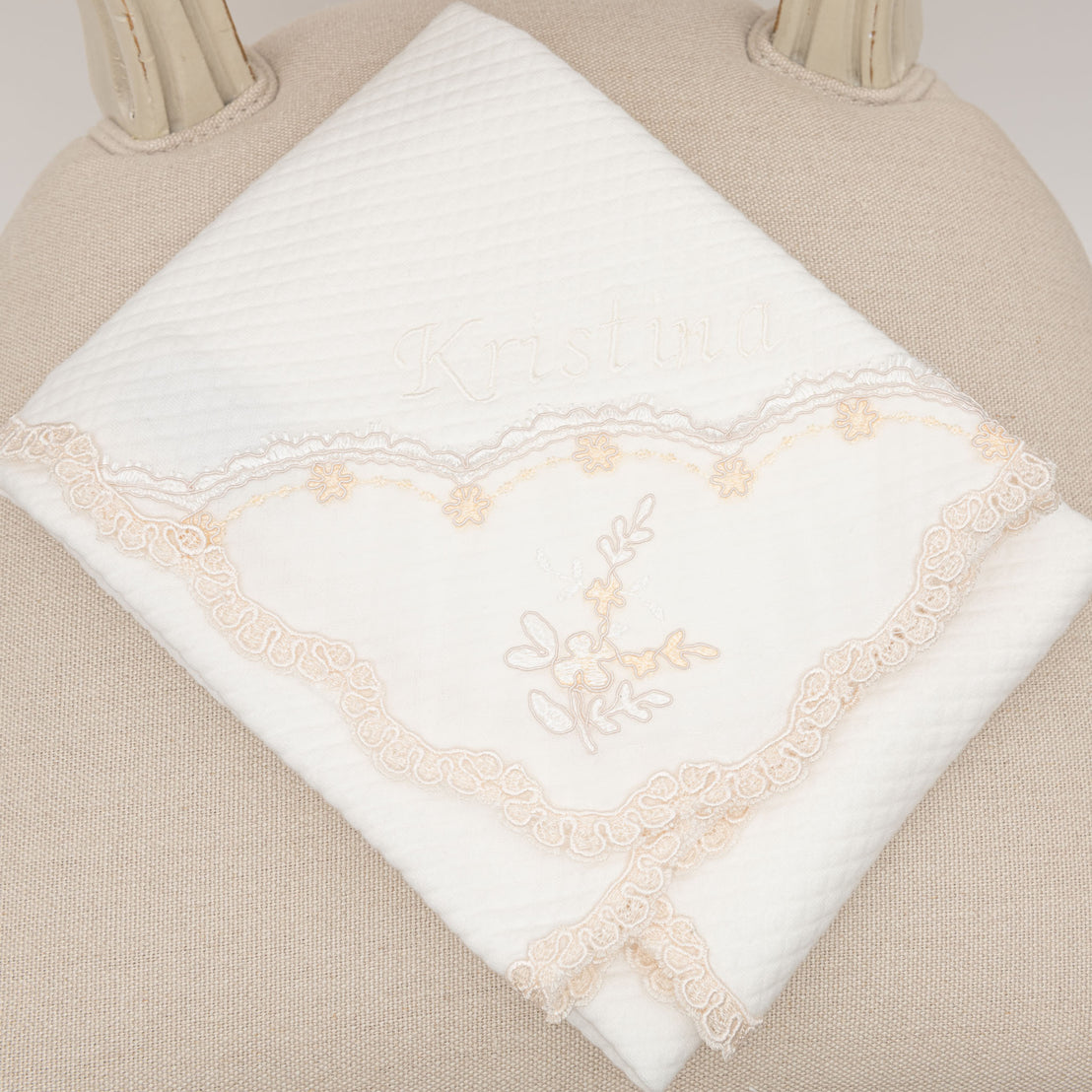 A close-up of a Kristina Blanket embroidered with the name "kristina" and destined to become an heirloom, surrounded by a lace heart, featuring a delicate floral design.