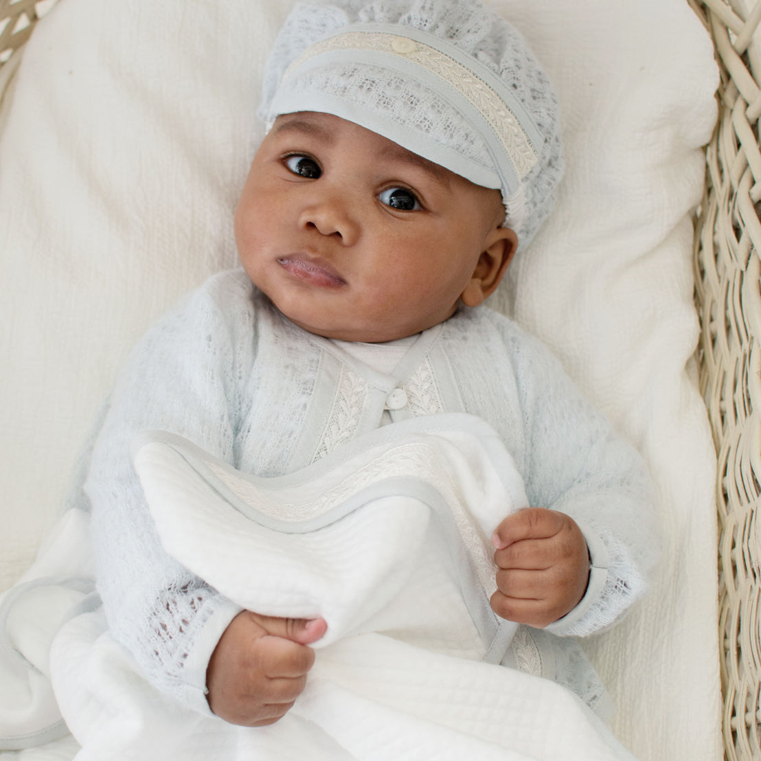Photo of baby in a crib wearing the Harrison Knit Sweater and Hat and holding the Harrison Personalized Blanket