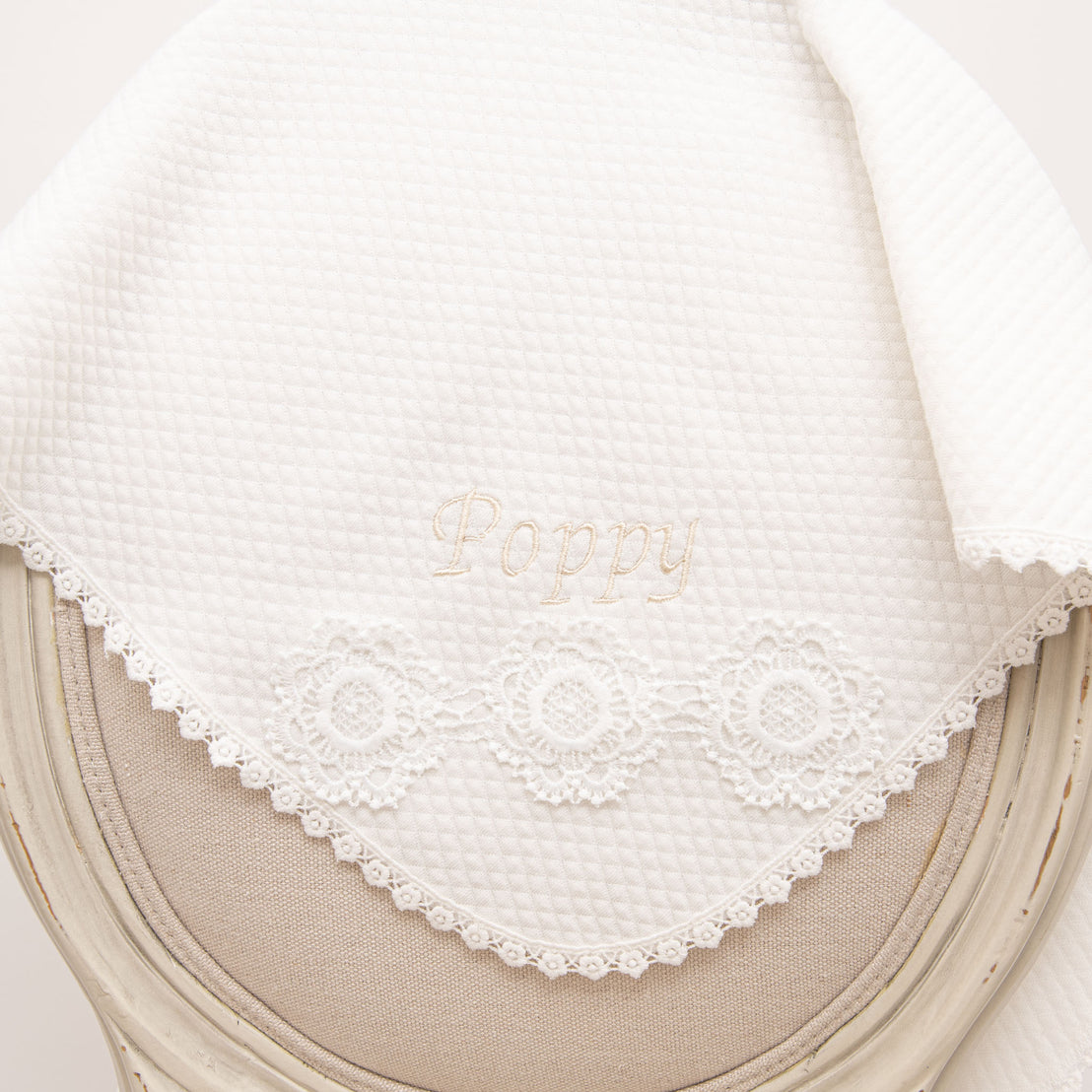 Poppy Personalized Blanket draped over a chair, featuring embroidered 'Poppy' lettering, floral lace detailing, and soft quilted fabric.